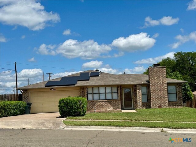 ranch-style home with driveway, brick siding, a garage, roof mounted solar panels, and a front yard