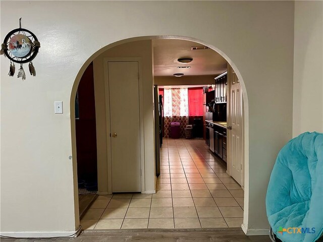 hallway featuring arched walkways, light tile patterned flooring, and visible vents