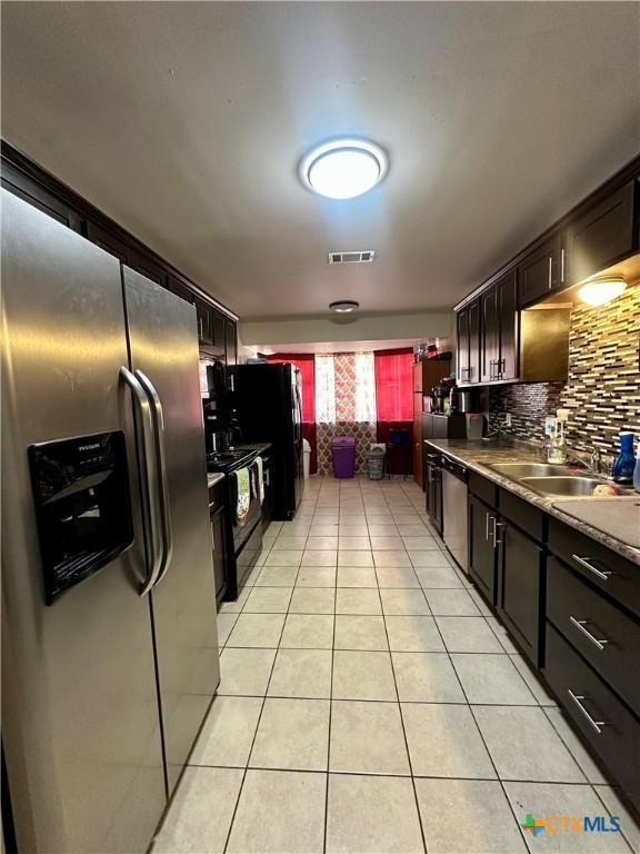 kitchen with stainless steel appliances, a sink, visible vents, backsplash, and light tile patterned floors