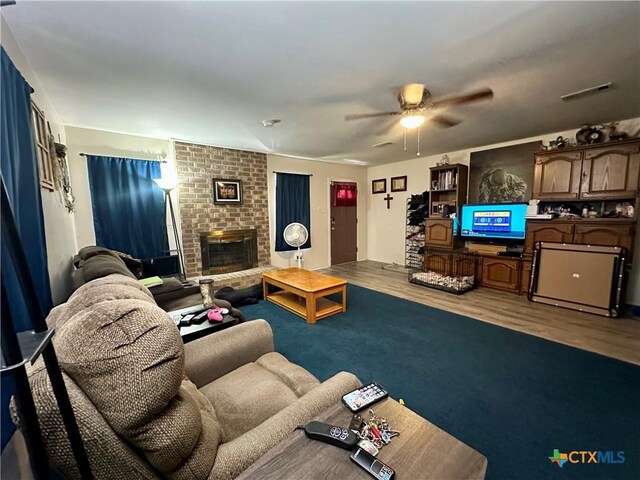 living room featuring ceiling fan, a brick fireplace, wood finished floors, and visible vents