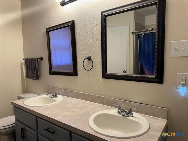 bathroom with toilet, a sink, and double vanity