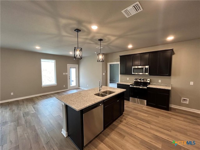 kitchen with sink, hanging light fixtures, stainless steel appliances, light hardwood / wood-style floors, and an island with sink