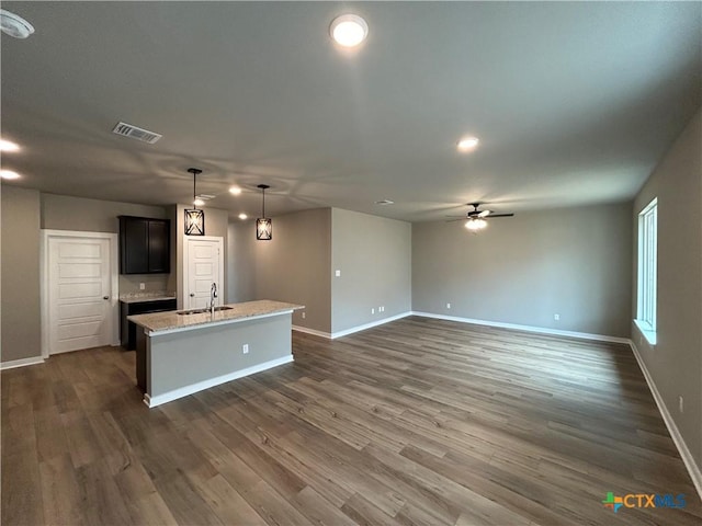 kitchen featuring decorative light fixtures, an island with sink, sink, light stone countertops, and dark wood-type flooring