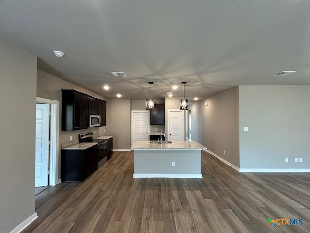 kitchen with sink, a center island with sink, appliances with stainless steel finishes, dark hardwood / wood-style floors, and light stone countertops