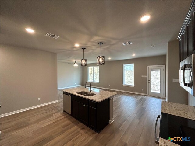 kitchen with sink, hardwood / wood-style flooring, appliances with stainless steel finishes, a kitchen island with sink, and hanging light fixtures