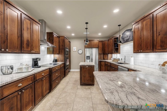 kitchen with light stone counters, wall chimney exhaust hood, stainless steel appliances, sink, and hanging light fixtures