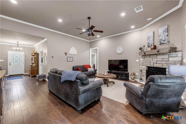 living room featuring ceiling fan with notable chandelier, dark hardwood / wood-style flooring, a stone fireplace, and crown molding