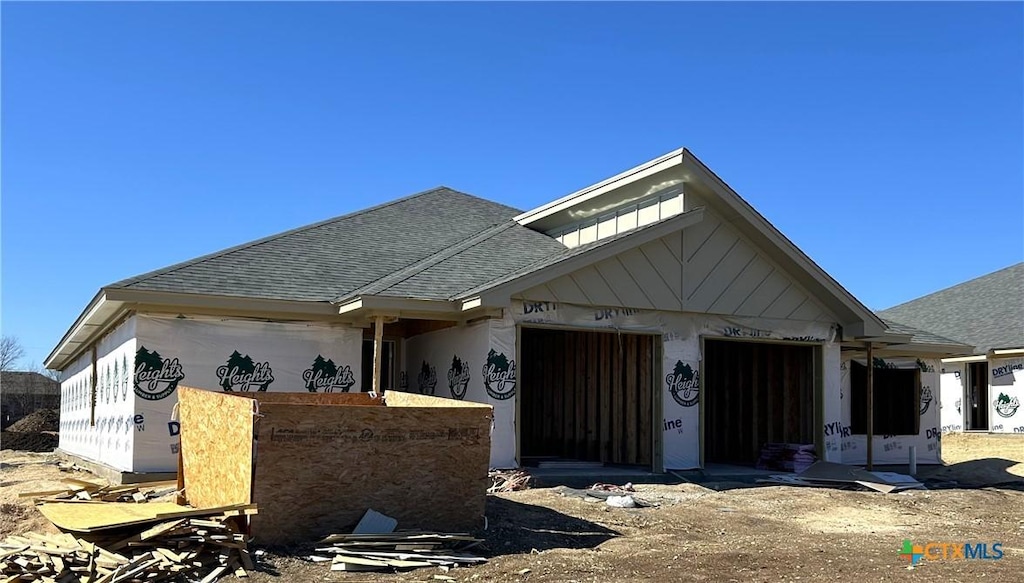 property under construction featuring stucco siding, an attached garage, roof with shingles, and dirt driveway