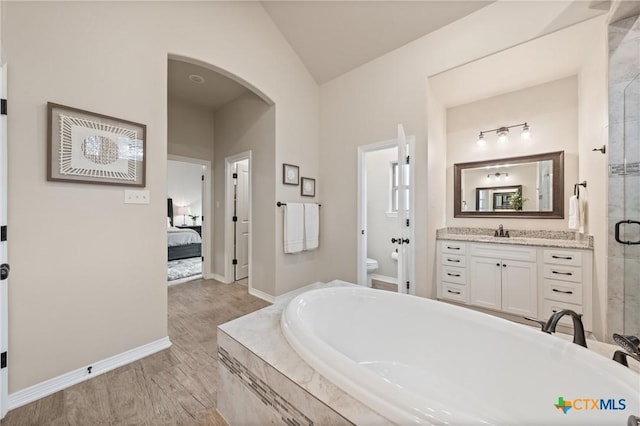 bathroom featuring lofted ceiling, toilet, a washtub, wood finished floors, and baseboards