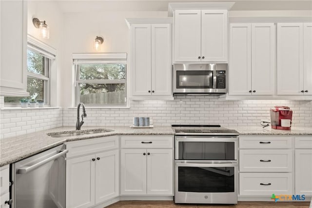 kitchen featuring white cabinets, appliances with stainless steel finishes, a sink, light stone countertops, and backsplash