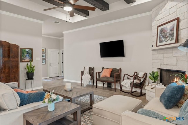 living area with a stone fireplace, a ceiling fan, baseboards, visible vents, and crown molding