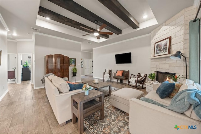 living room with light wood-style floors, visible vents, crown molding, and a stone fireplace