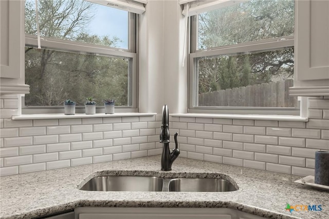 kitchen with a sink, backsplash, and light stone countertops