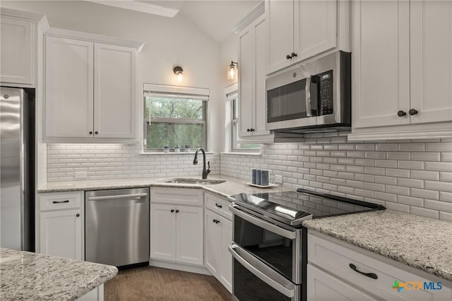 kitchen with tasteful backsplash, white cabinets, lofted ceiling, appliances with stainless steel finishes, and a sink