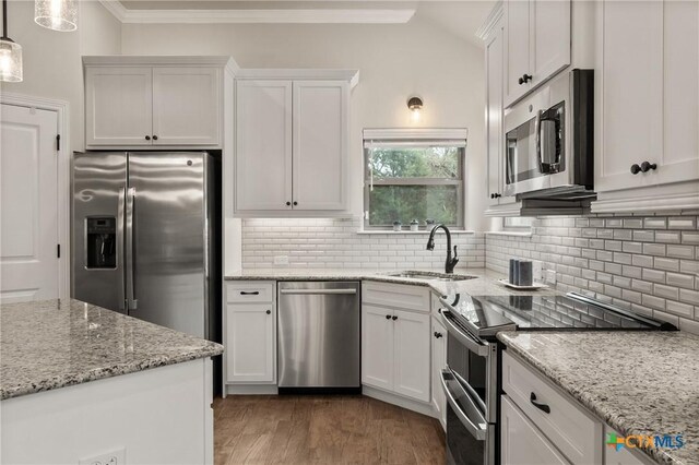 kitchen with appliances with stainless steel finishes, white cabinetry, a sink, and ornamental molding