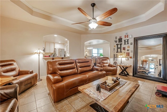 living area featuring arched walkways, a tray ceiling, a ceiling fan, crown molding, and light tile patterned floors