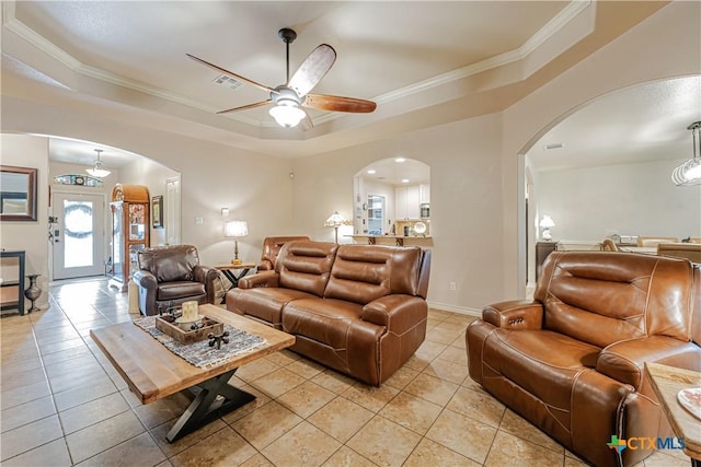 living area with arched walkways, a raised ceiling, a ceiling fan, light tile patterned floors, and ornamental molding