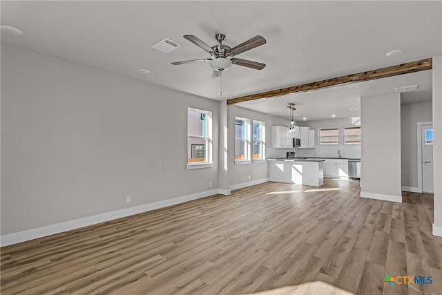 unfurnished living room with ceiling fan, beam ceiling, sink, and light hardwood / wood-style flooring