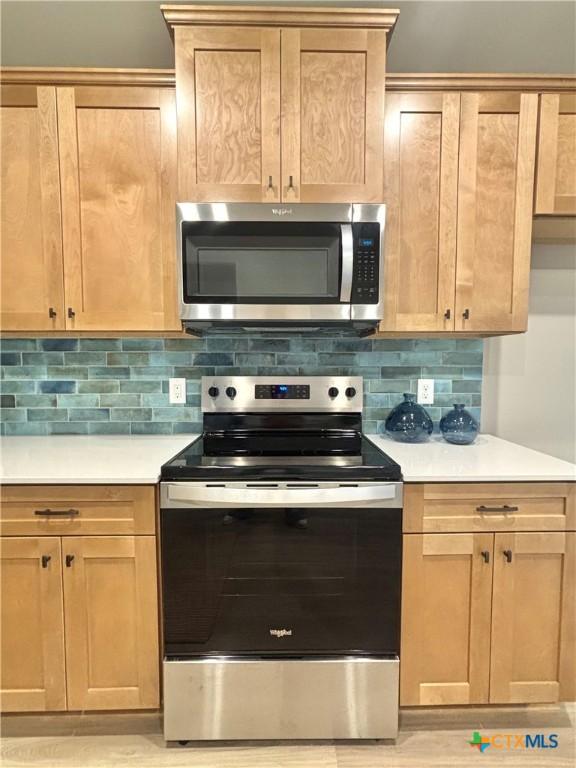 kitchen with stainless steel appliances, light brown cabinetry, light countertops, and decorative backsplash