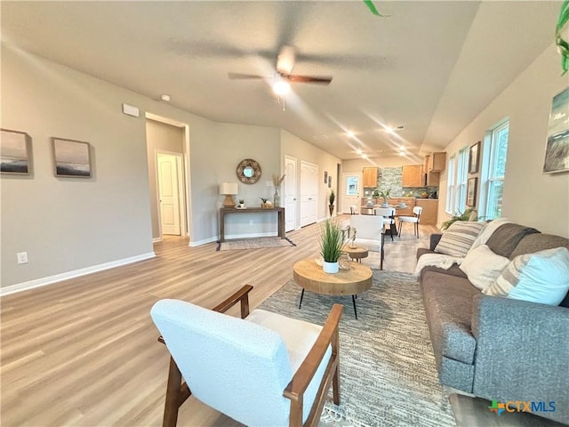 living room featuring a ceiling fan, light wood-type flooring, vaulted ceiling, and baseboards