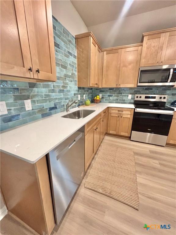 kitchen featuring stainless steel appliances, light countertops, decorative backsplash, light brown cabinetry, and a sink