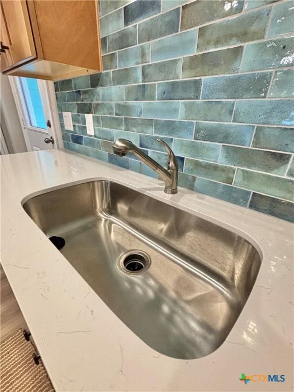 details featuring a sink, light stone counters, backsplash, and brown cabinets