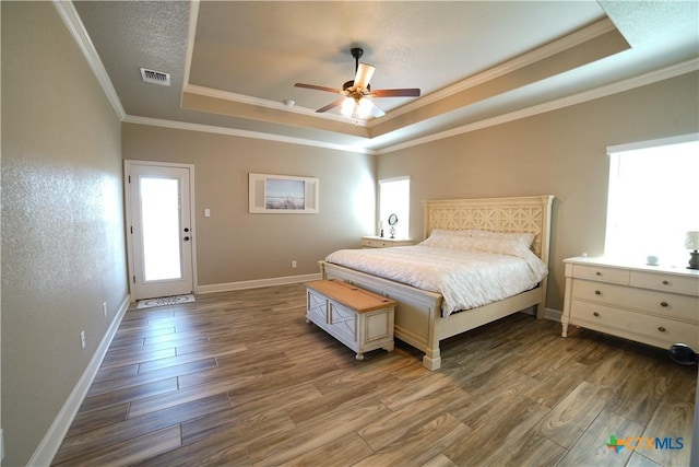 bedroom featuring visible vents, a raised ceiling, multiple windows, and wood finished floors