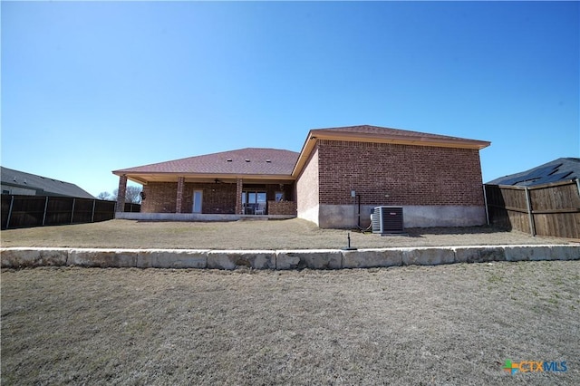 rear view of property featuring brick siding, a lawn, cooling unit, and fence