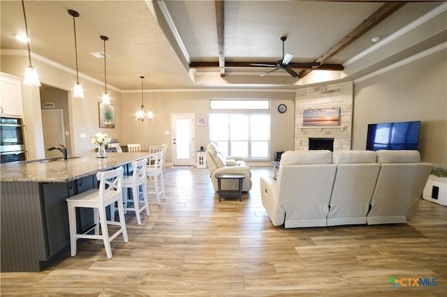 living area featuring a fireplace, crown molding, light wood-style flooring, and ceiling fan with notable chandelier