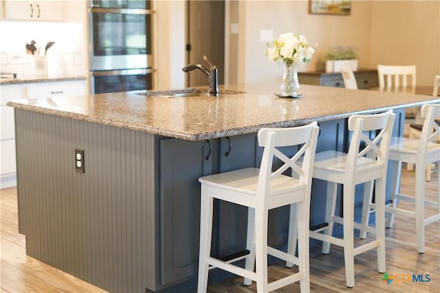 kitchen featuring light stone countertops, double oven, and light wood-style flooring