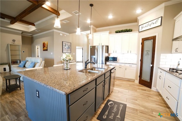 kitchen with light wood finished floors, backsplash, appliances with stainless steel finishes, white cabinets, and a sink