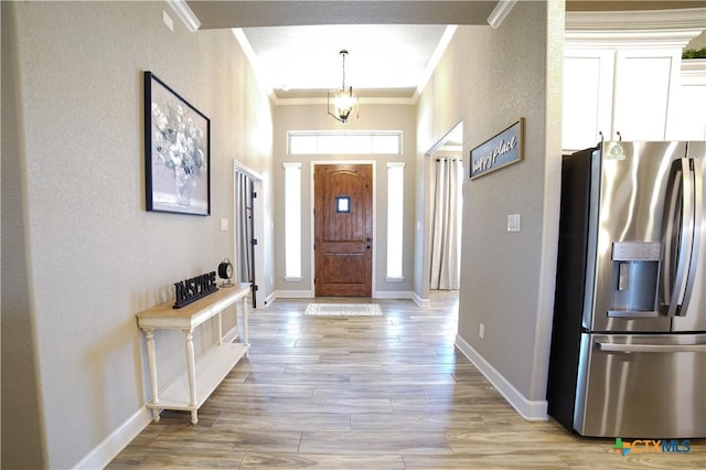 foyer entrance with light wood-type flooring, baseboards, ornamental molding, and a textured wall