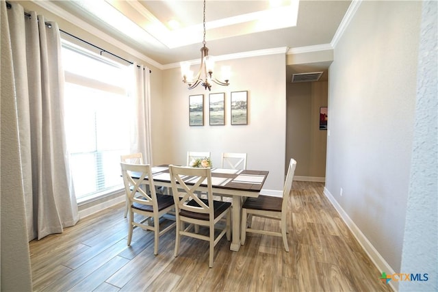 dining room with wood finished floors, baseboards, crown molding, a raised ceiling, and a chandelier