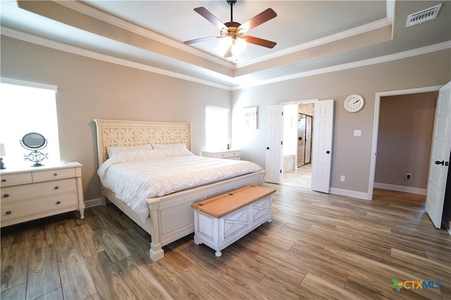 bedroom with a tray ceiling, visible vents, and wood finished floors