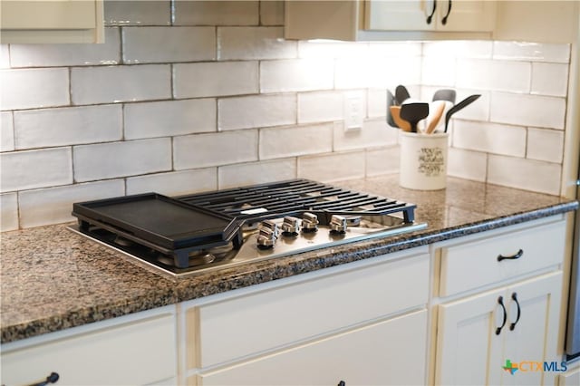 kitchen featuring stainless steel gas cooktop, decorative backsplash, dark stone countertops, and white cabinetry