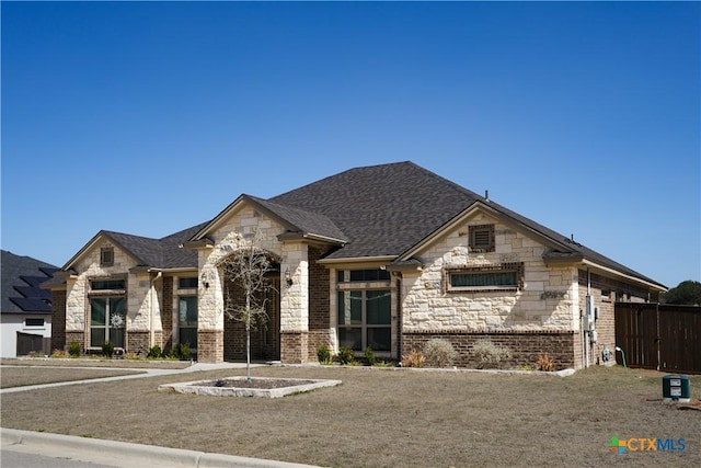 french country style house featuring fence, brick siding, stone siding, and a shingled roof