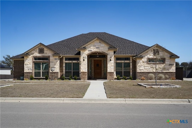 french country home with brick siding, stone siding, and a shingled roof