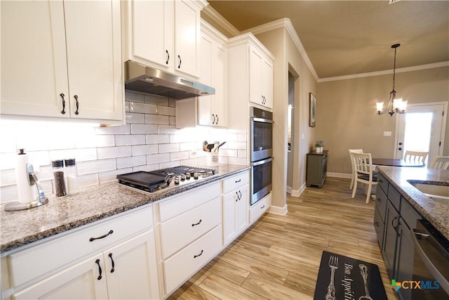 kitchen with ornamental molding, under cabinet range hood, white cabinetry, appliances with stainless steel finishes, and light stone countertops