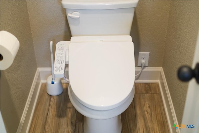 bathroom with toilet, a textured wall, and wood finished floors