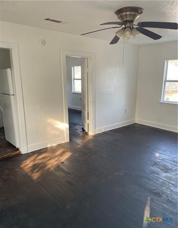 spare room featuring a textured ceiling, ceiling fan, and dark wood-type flooring