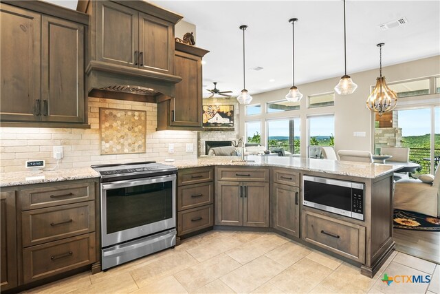 kitchen featuring stainless steel appliances, ceiling fan with notable chandelier, backsplash, a peninsula, and a stone fireplace