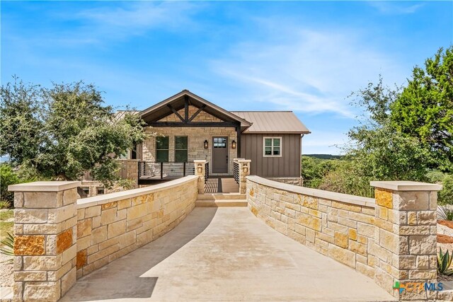 view of front of house with metal roof, a porch, stone siding, and board and batten siding