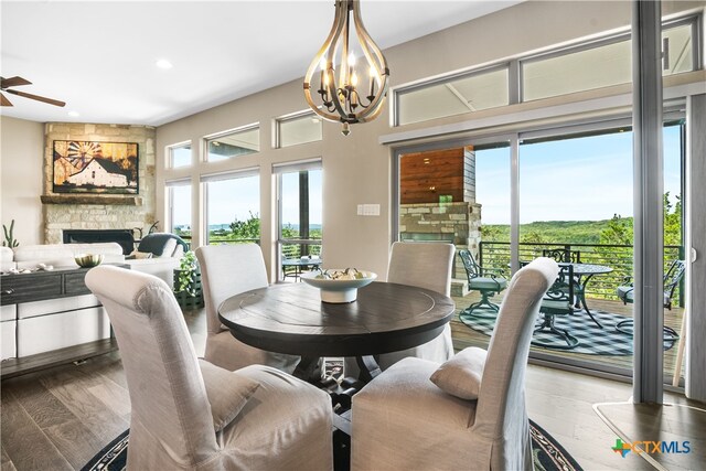 dining space with ceiling fan with notable chandelier, a healthy amount of sunlight, a fireplace, and wood finished floors