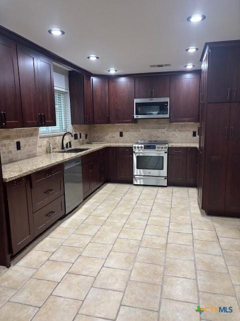 kitchen with a sink, stainless steel appliances, light stone counters, visible vents, and backsplash