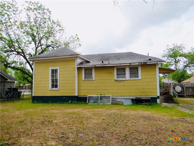 back of house featuring a yard, roof with shingles, and fence