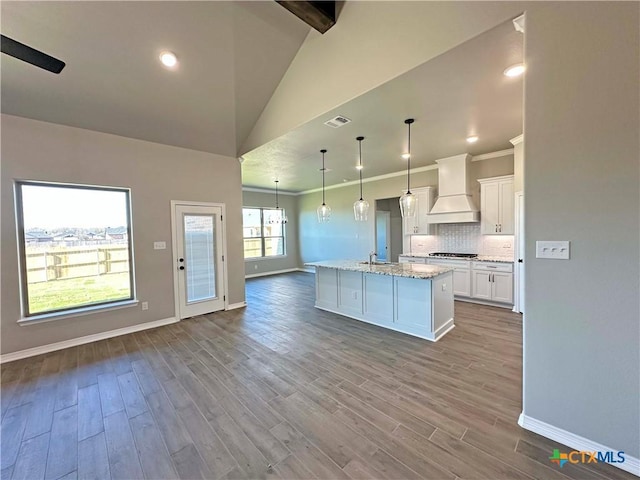 kitchen featuring custom exhaust hood, white cabinets, light hardwood / wood-style flooring, an island with sink, and decorative light fixtures