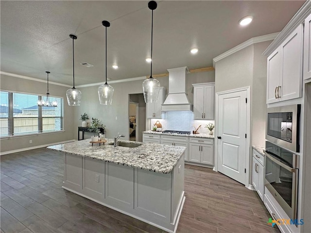 kitchen featuring a center island with sink, stainless steel appliances, custom exhaust hood, white cabinets, and pendant lighting