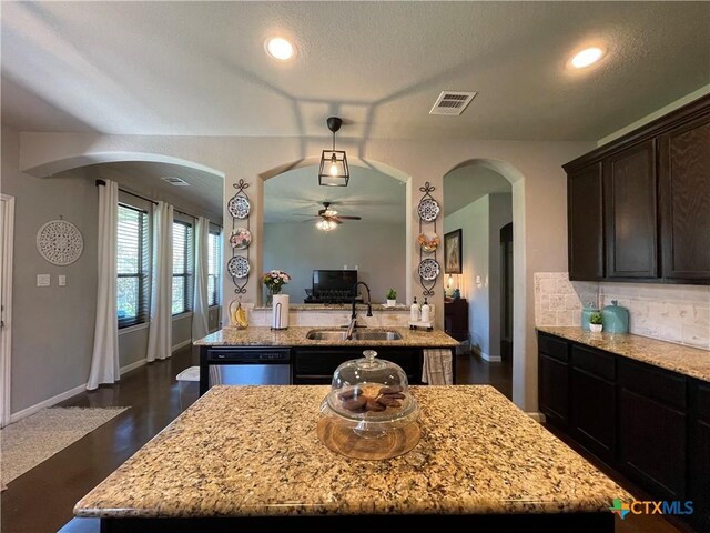 kitchen with light stone countertops, dark brown cabinets, a textured ceiling, stainless steel appliances, and a center island