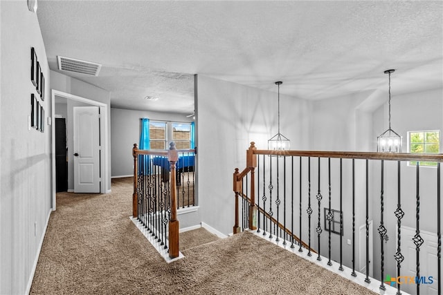 hallway with carpet flooring, a textured ceiling, and a notable chandelier