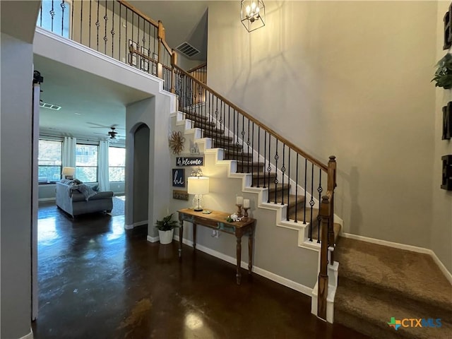 staircase featuring arched walkways, a high ceiling, visible vents, and baseboards